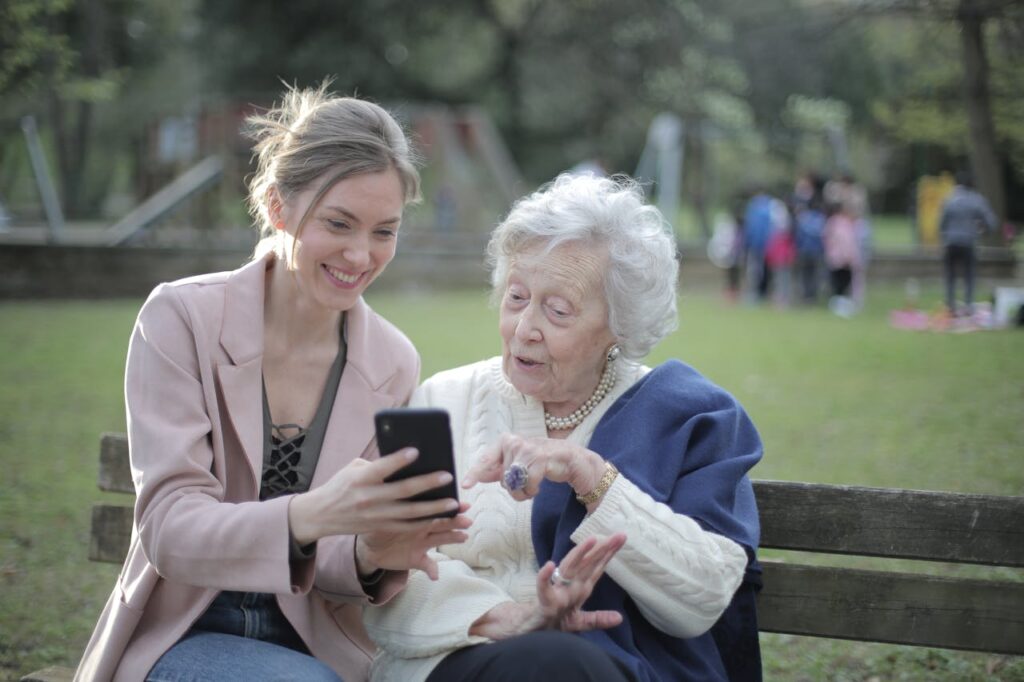 pexels photo 3791664 Delighted female relatives sitting together on wooden bench in park and browsing mobile phone while learning using